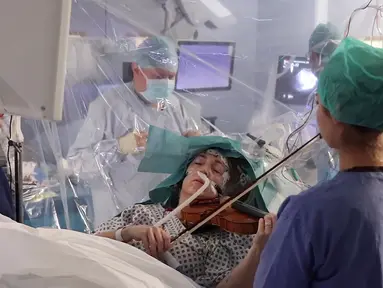 Gambar yang direkam pada 31 Januari 2020, musisi Dagmar Turner bermain biola saat berlangsungnya operasi pengangkatan tumor otak di King's College Hospital, London. Ini dilakukan untuk mempertahankan keahlian Turner dalam bermain biola, hobinya sejak usia 10 tahun. (KING'S COLLEGE HOSPITAL/AFP)