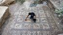 Putra petani Palestina Salman al-Nabahin membersihkan mosaik era Bizantium yang ditemukan di Bureij, Jalur Gaza, Palestina, 18 September 2022. "Ini adalah lantai mosaik terindah yang ditemukan di Gaza, baik dari segi kualitas representasi grafis maupun kompleksitas geometrinya," kata Arkeolog René Elter. (MOHAMMED ABED/AFP)