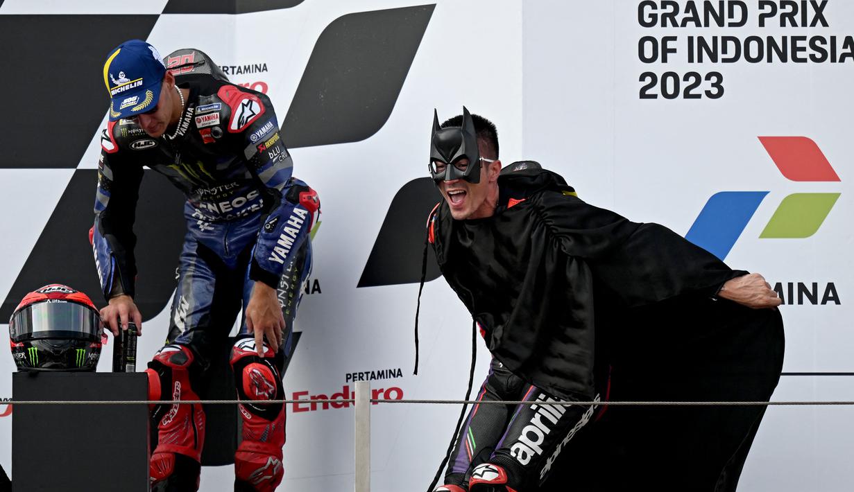 Pembalap Aprilia Racing, Maverick Vinales (kanan), memakai kostum Batman saat menaiki podium juara MotoGP Mandalika 2023 setelah menjalani balapan di Mandalika International Street Circuit, Lombok, Minggu (15/10/2023) siang WIB. (AFP/Sonny Tumbelaka)