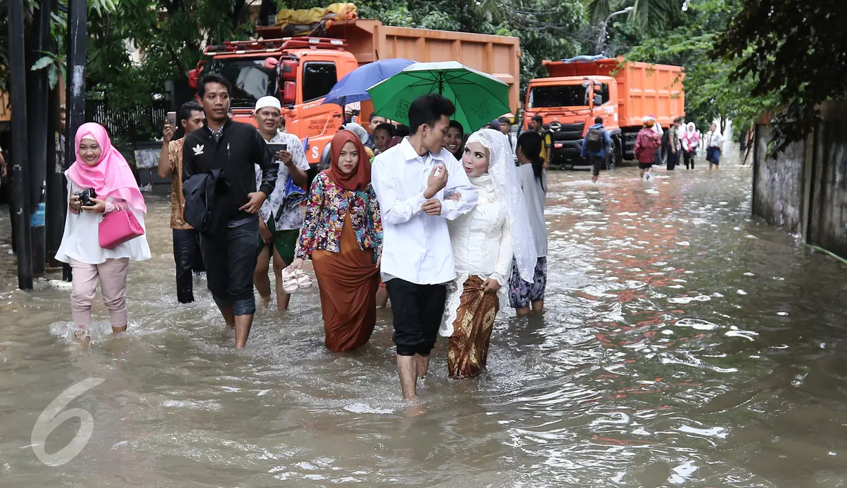 Pengantin Mansur dan Maya melintasi banjir usai melakukan akad nikah di KUA Mampang Prapatan, Jakarta, Selasa (21/2). Walapun banjir sepasang pengantin ini tetap melakukan akad nikah. (Liputan6.com/Herman Zakharia)