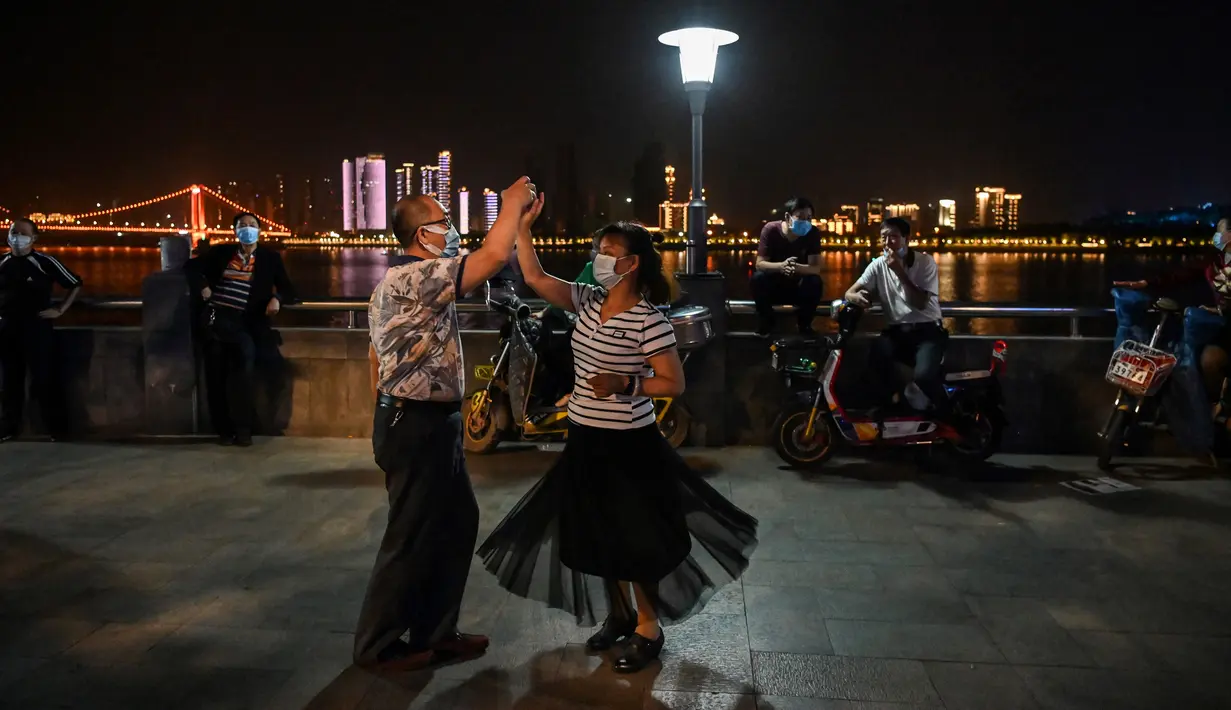 Pasangan mengenakan masker menari di sebuah taman di sebelah Sungai Yangtze, Wuhan, provinsi Hubei tengah China (12/5/2020). China dua hari berturut-turut mengalami peningkatan dua digit kasus virus corona yang kembali muncul di Wuhan pada pekan lalu. (AFP/Hector Retamal)