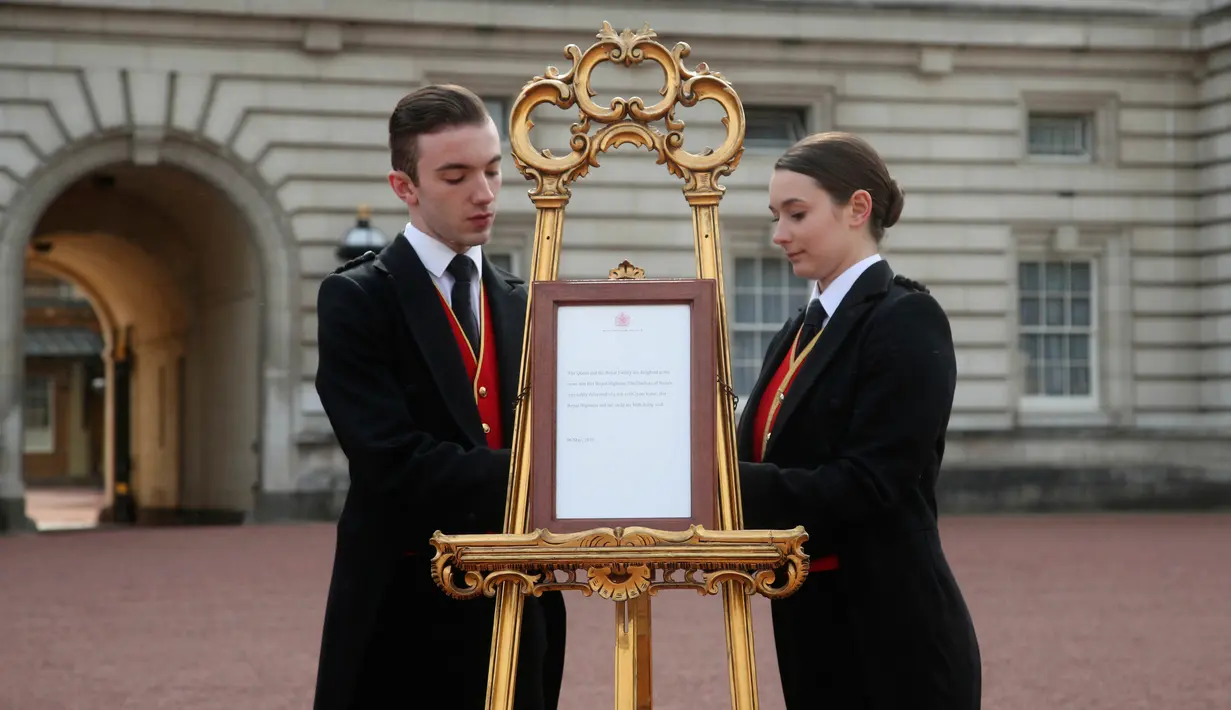 Pelayan kerajaan Stephen Kelly dan Sarah Thompson membawa papan pengumuman kelahiran anak pertama Pangeran Harry dan Meghan Markle di London, Inggris, Senin (6/5/2019). Dalam tradisi kerajaan, setiap kelahiran bayi akan diumumkan di depan Istana Buckhingham. (Yui Mok/Pool Photo via AP)