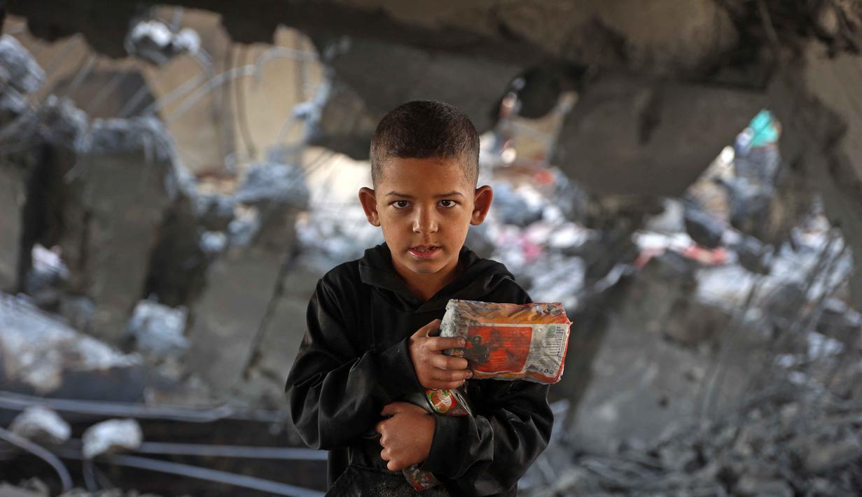 Sejak dimulainya gencatan senjata yang rapuh itu, sedikitnya 280 warga Palestina tewas dan lebih dari 670 orang luka-luka akibat serangan Israel. Sementara laporan sebelumnya dari otoritas kesehatan Gaza, terdapat hampir 70.000 orang tewas sejak konflik pecah dua tahun lalu. Tampak dalam foto, seorang anak laki-laki Palestina memegang barang-barangnya di tengah puing-puing bangunan yang rusak milik Kementerian Wakaf Agama, yang menjadi tempat penampungan bagi pengungsi di kawasan Zeitoun, Kota Gaza, pada Kamis 20 November 2025, sehari setelah bangunan tersebut menjadi sasaran serangan militer Israel. (Omar AL-QATTAA /AFP)