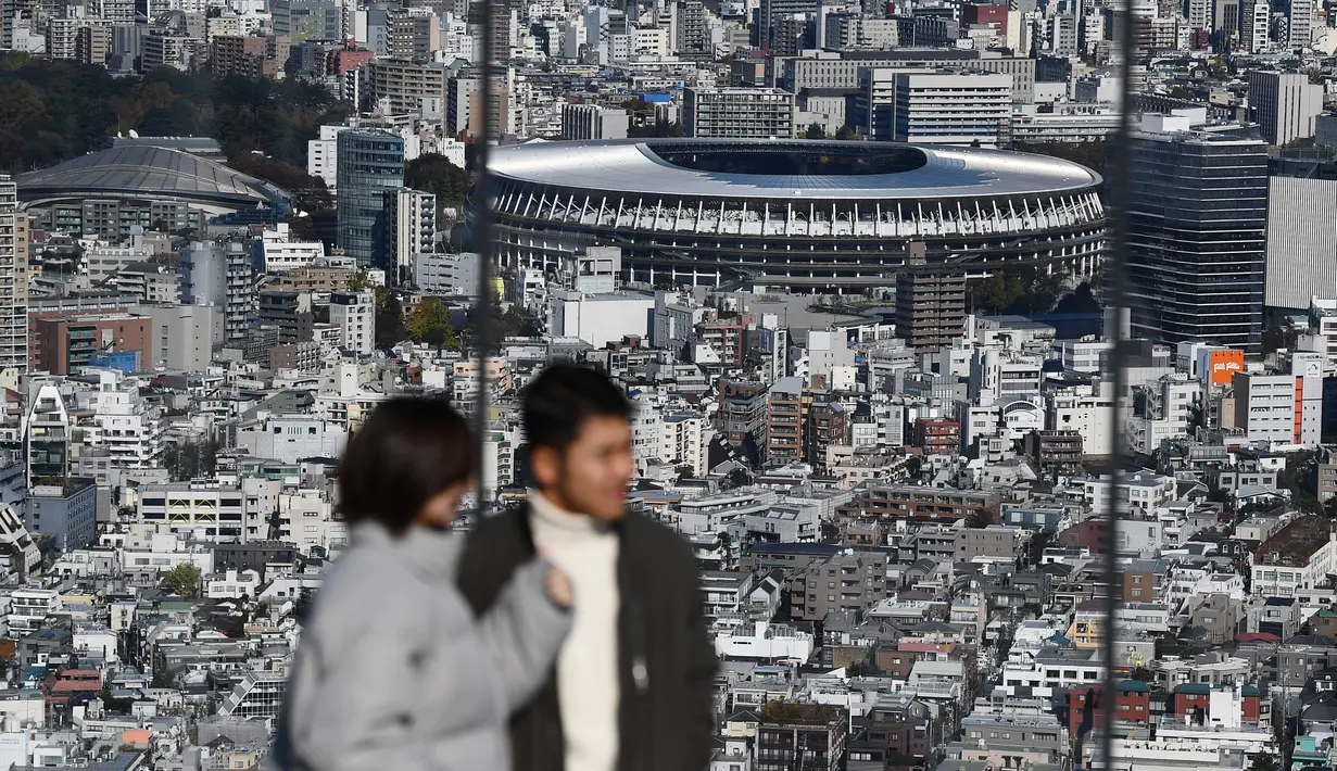 Orang-orang melihat Stadion Nasional Tokyo untuk Olimpiade dan Paralimpiade Tokyo 2020 setelah selesai direnovasi di Tokyo (30/11/2019). Stadion tersebut didesain oleh arsitek Jepang, Kengo Kuma, dan konstruksinya mewakili koneksi Jepang dengan alam bebas. (AFP Photo/Charly Triballeau)