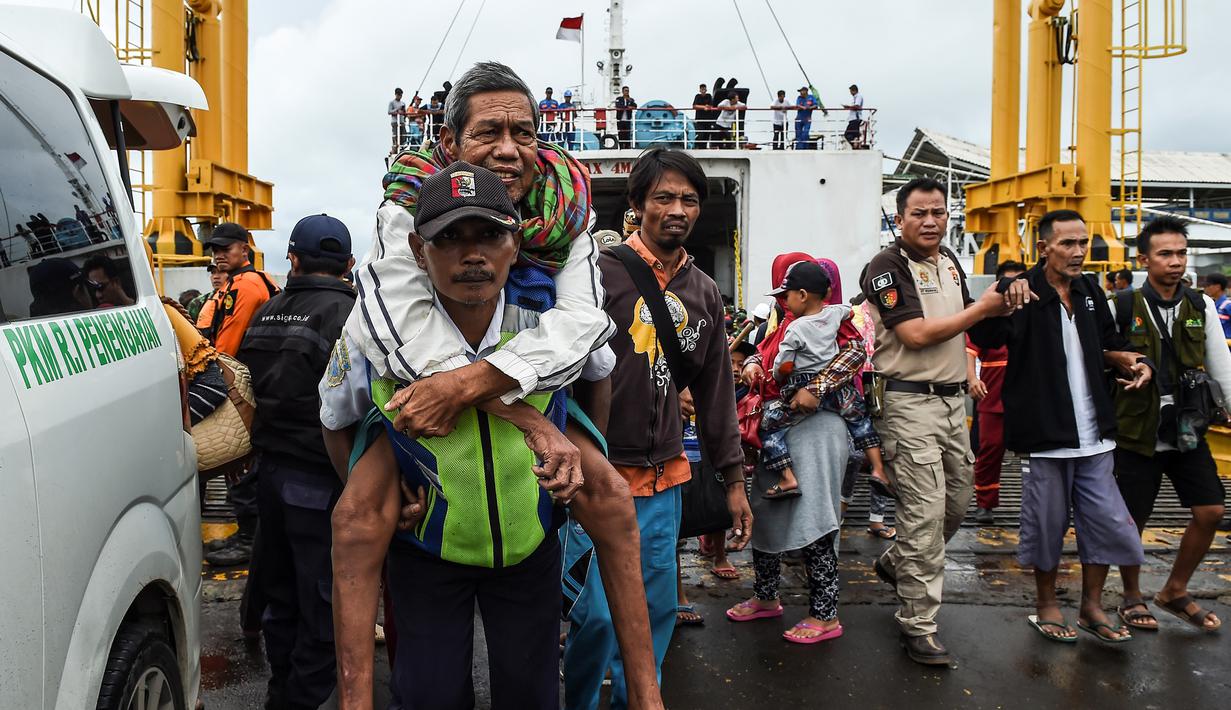 Petugas menggendong pengungsi usai turun dari kapal ferry di Pelabuhan Bakauheni, Lampung (26/12). Aktivitas gunung berapi anak Krakatau yang mengakibatkan gelombang tsunami 22 Desember lalu memaksa belasan ribu orang mengungsi. (AFP Photo/Mohd Rasfan)