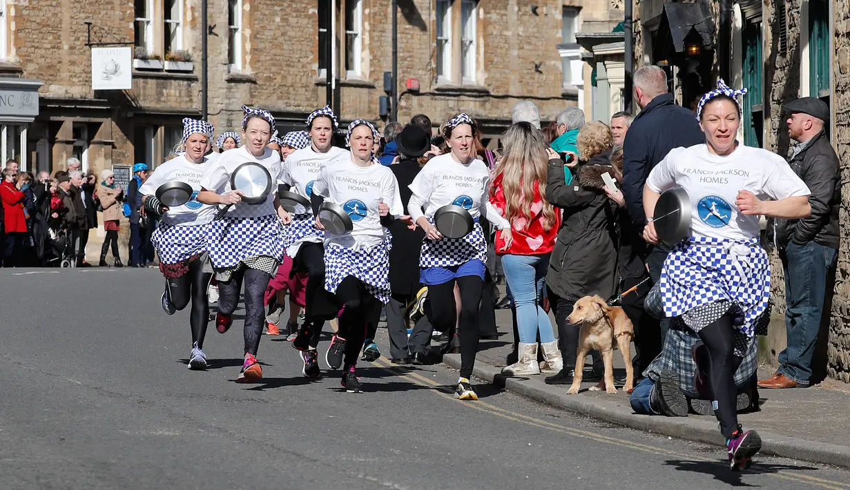 Amy Butler berlari memimpin lomba lari dengan membawa pancake dalam lomba tahunan Pancake Trans-Atlantic di kota Olney, Buckinghamshire, Inggris, Selasa (5/3). Peserta juga harus membolak-balikan pancake sambil tetap berlari. (AP/Frank Augstein)