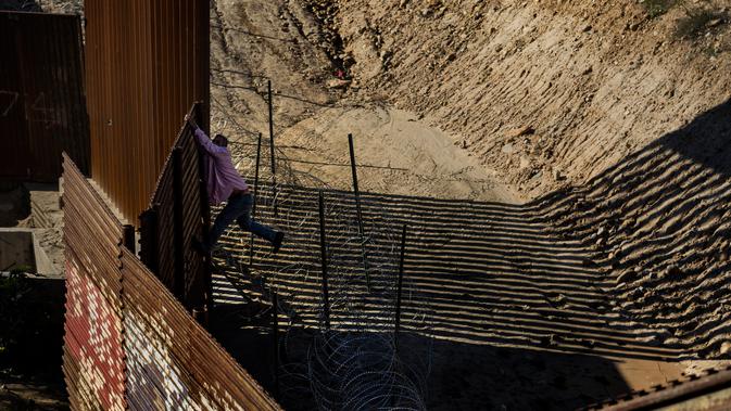 Seorang imigran dengan kemejanya yang sobek berusaha memanjat pagar perbatasan dari Tijuana, Meksiko untuk masuk ke sisi AS ke San Diego, California, (28/12). (AP Photo/Daniel Ochoa de Olza)