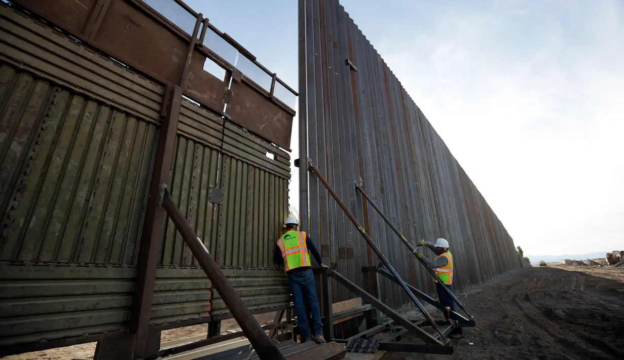 Pekerja melihat di antara pagar perbatasan Amerika Serikat (AS) dengan Meksiko di Calexico, California, AS, Minggu (5/3). Pembangunan tembok pembatas di area ini sudah direncanakan sejak zaman Barack Obama tahun 2009. (AP Photo/Gregory Bull)