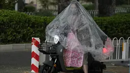 Seorang wanita bermasker menggunakan plastik besar untuk menutupi tubuhnya saat hujan di Beijing (24/5/2022). Beijing memperpanjang perintah bagi pekerja dan pelajar untuk tinggal di rumah dan memerintahkan pengujian massal tambahan pada Senin ketika kasus COVID-19 meningkat di ibu kota China. (AP Photo/Ng Han Guan)