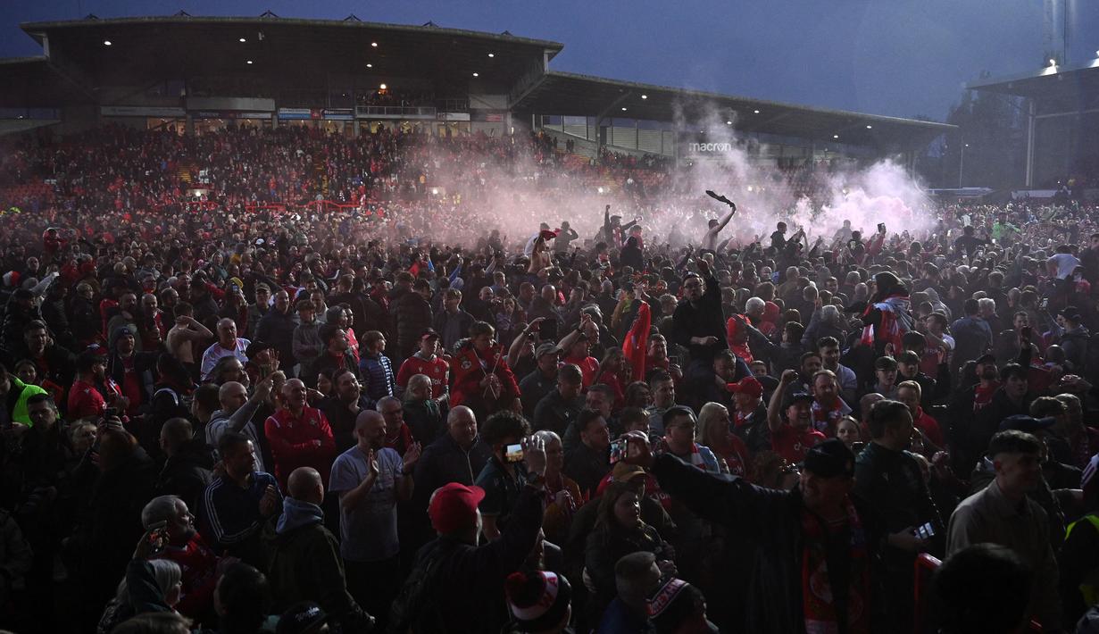 Pendukung Wrexham merayakan kemenangan timnya saat laga English National League antara Wrexham melawan Boreham Wood di Racecourse Ground Stadium, Wrexham, Wales, Sabtu (22/04/2023). Wrexham menang dengan skor 3-1 dan berhasil promosi ke Liga Dua Inggris. (AFP/Oli Scarff)