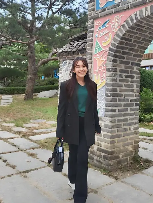 Ayu Ting Ting mengenakan blazer hitam oversize senada dengan celana flare dan handbag. Ia juga mengenakan inner knit hijau. [@ayutingting92]