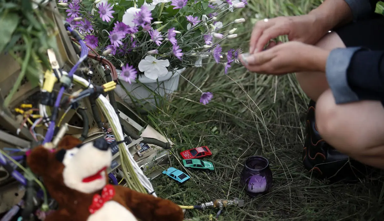 Salah satu warga meletakkan untaian bunga dan mainan anak di dekat lokasi jatuhnya pesawat Malaysia Airlines MH-17 di Donetsk, Ukraina, (19/7/2014). (REUTERS/Maxim Zmeyev)