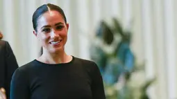Meghan Markle tersenyum saat tiba di markas PBB (18/7/2022). Duchess of Sussex tampil dengan outfit of the day (OOTD) blus hitam lengan tiga perempat merek Givenchy dipadu rok yang senada. (AFP Photo/Kena Betancur)
