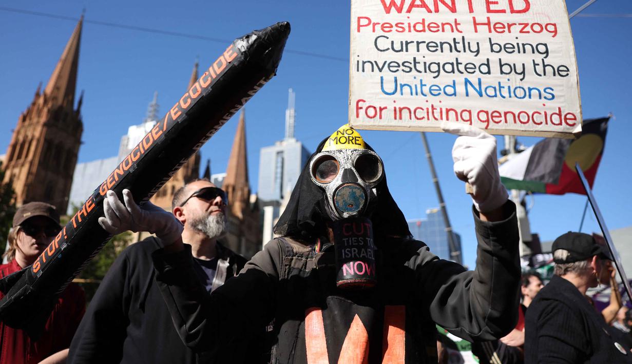 Sebagai informasi, kunjungan Presiden Israel, Isaac Herzog, terjadi setelah gencatan senjata menghentikan serangan Israel ke Gaza yang dimulai pada Oktober 2023. Tampak dalam foto, para pengunjuk rasa memegang bendera dan spanduk di luar stasiun Flinders Street selama kunjungan Presiden Israel, Isaac Herzog, di Melbourne, Australia, Kamis (12/2/2026). (MARTIN KEEP/AFP)