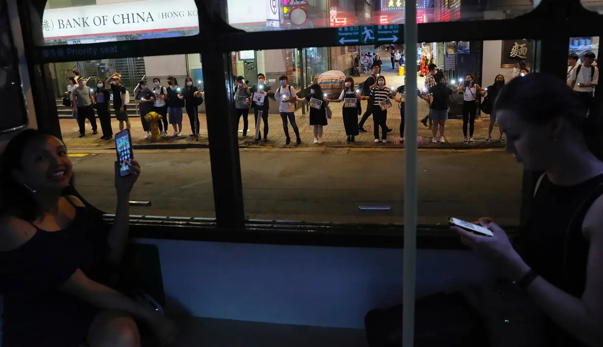 Demonstran prodemokrasi terlihat dari dalam trem sedang membentuk rantai manusia di jalanan Hong Kong, Jumat (23/8/2019). Dengan bergandengan tangan dan menyanyikan lagu-lagu, puluhan ribu demonstran berjejer di trotoar, jembatan layang, dan taman-taman Hong Kong. (AP Photo/Kin Cheung)