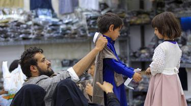 Warga Yaman membantu memilihkan pakaian baru untuk anak-anak mereka di ruang pamer yang membagikan pakaian kepada para pemuda yang kehilangan orang tua dalam konflik, sebagai bagian dari kegiatan amal selama bulan suci Ramadhan, di ibu kota Sanaa (8/4/2022). (AFP/Mohammed Huwais)