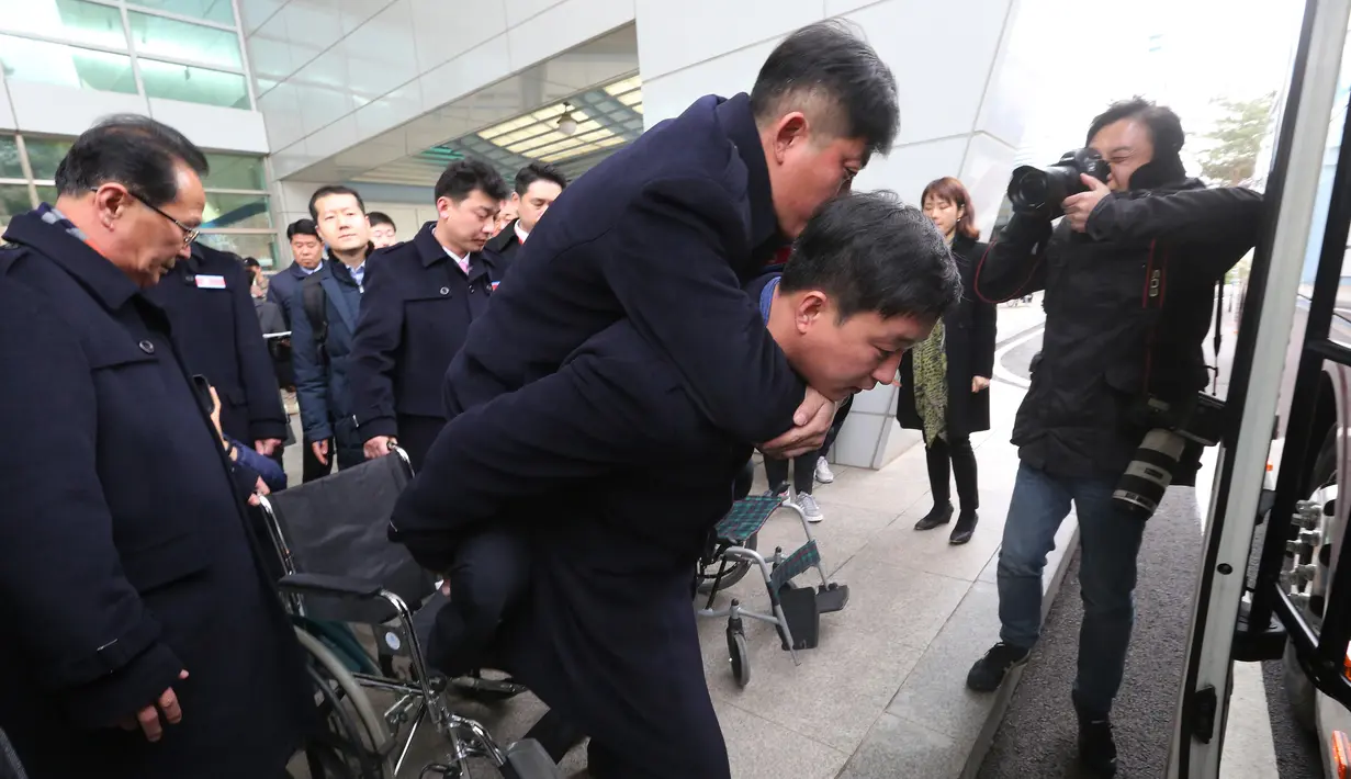 Seorang pria menggendong atlet Paralimpiade Pyeongchang 2018 asal Korea Utara yang hendak menaiki bus usai tiba di Paju, Korea Selatan, Rabu (7/3). Kontingen Korea Utara akan kembali ke negaranya pada 15 Maret. (Ahn Young-joon/POOL/AFP)