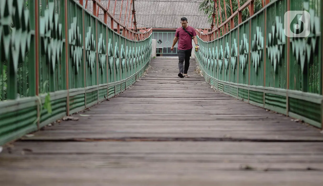 Warga berjalan melintasi jembatan yang berlubang di Jembatan Wiratman, Srengseng Sawah, Jakarta, Sabtu (12/3/2022). Jembatan tersebut menghubungkan Kelurahan Srengseng Sawah, Jakarta Selatan dengan Kelurahan Pasir Gunung Selatan, Depok. (Liputan6.com/Herman Zakharia)