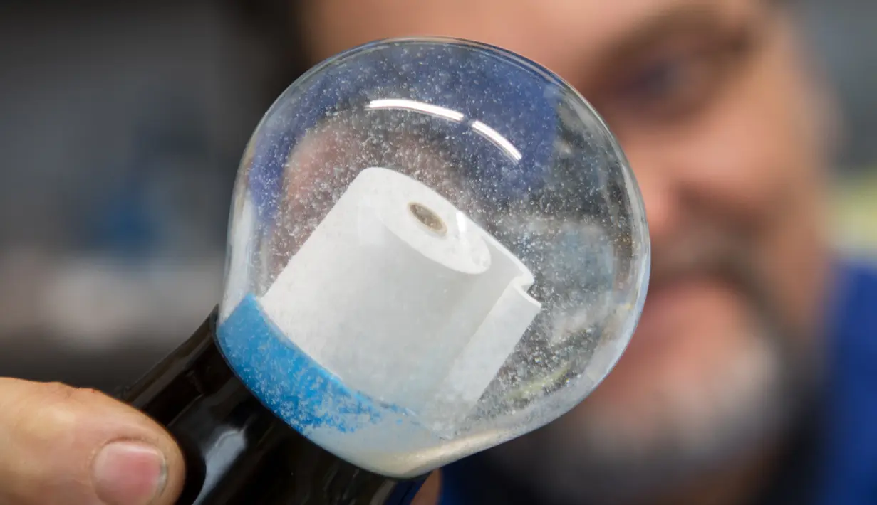 Pemilik perusahaan Original Vienna Snow Globes, Erwin Perzy III memegang bola salju yang berisi gulungan kertas toilet di Wina, Austria, pada 17 April 2020. Bola salju yang memiliki desain istimewa ini terinspirasi dari panic buying pada awal virus corona Covid-19. (ALEX HALADA/AFP)