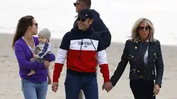 Presiden Prancis Emmanuel Macron dan istrinya Brigitte Macron berbincang dengan seorang wanita yang menggendong anaknya saat mereka berjalan di sepanjang pantai di Le Touquet, Sabtu (23/4/2022). Emmanuel Macron akan menghadapi Marine Le Pen dalam putaran kedua pemilihan presiden (pilpres) pada 24 April 2022. (Ludovic MARIN / AFP)