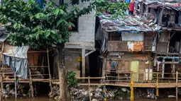Kepadatan yang sangat tinggi ini disebabkan oleh faktor urbanisasi yang terus meningkat, menjadikan Jakarta sebagai pusat ekonomi dan bisnis nasional. Tampak dalam foto, seorang pria berdiri di atas jembatan bambu yang menghubungkan rumah-rumah di permukiman kumuh tepi sungai yang padat penduduk di Jakarta pada Selasa 21 April 2026. (BAY ISMOYO/AFP)