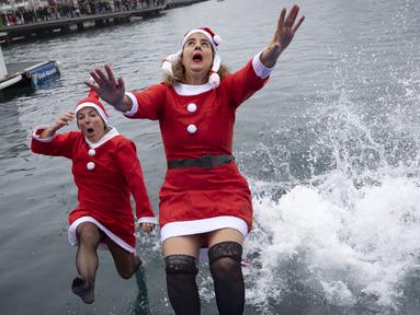 Sejumlah peserta berkostum Sinterklas melompat ke dalam air dalam ajang Copa Nadal yang berlangsung di Barcelona's Port Vell, Barcelona, Kamis (25/12/2025) waktu setempat. Acara tersebut diikuti lebih dari 450 peserta. (AFP/Josep Lago)