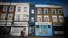 Seorang pejalan kaki melewati bagian depan bangunan yang dijuluki "Rumah Tersempit di London" (cat biru) di London barat pada 5 Februari 2021. Terjepit di antara praktek dokter dan salon penata rambut, rumah mungil tersebut hanya memiliki lebar 1,6 meter dan panjang 7,31 meter. (Tolga Akmen/AFP)
