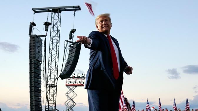 Presiden Donald Trump melemparkan masker dari atas panggung ke kerumunan pendukung saat berkampanye di Bandara Internasional Orlando Sanford di Sanford, Florida, Senin (12/10/2020). Donald Trump kembali berkampanye untuk pertama kalinya usai dinyatakan negatif Covid-19. (AP Photo/Evan Vucci)
