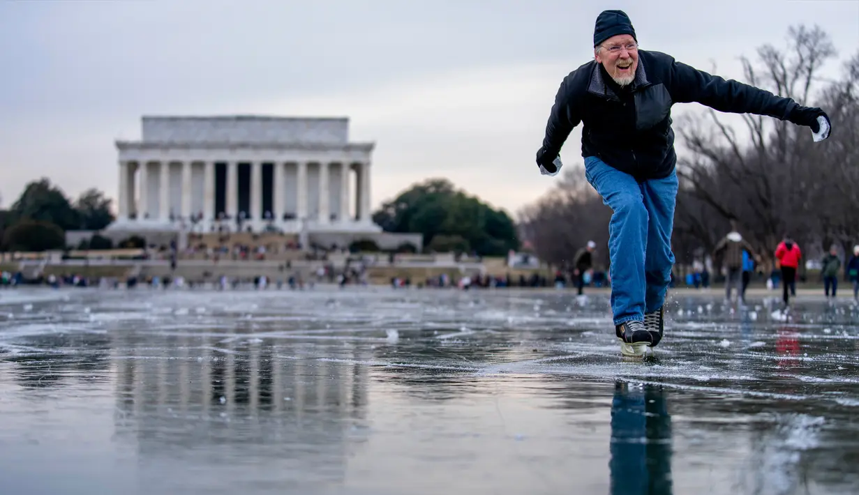 Lincoln Memorial terlihat saat Dan DeMocker dari Tacoma Park meluncurkan bongkahan es ke arah keluarganya saat ia berseluncur es di Reflecting Pool yang membeku di National Mall, Washington, Amerika Serikat, 26 Desember 2022. Selama akhir pekan, suhu beku menggoda banyak orang untuk bermain di Reflecting Pool. (AP Photo/Andrew Harnik)