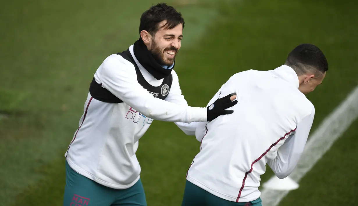 Gelandang Manchester City Bernardo Silva (kiri) bercanda dengan Phil Foden selama sesi latihan tim di City Football Academy di Manchester, barat laut Inggris (8/3/2022). Pada leg pertama babak 16 Liga Champions, City menang telak atas Sporting CP 5-0. (AFP/Oli Scarff)