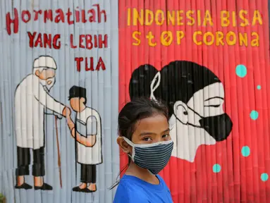 Seorang anak kenakan masker dengan latar belakang mural Indonesia Bisa Stop Corona di Lapangan Bulutangkis, Kampung Kali Pasir, Jakarta, Selasa (7/4/2020). Pesan mural mengajak warga untuk memutus rantai penyebaran Corona Covid-19 dengan diam di rumah. (Liputan6.com/Fery Pradolo)