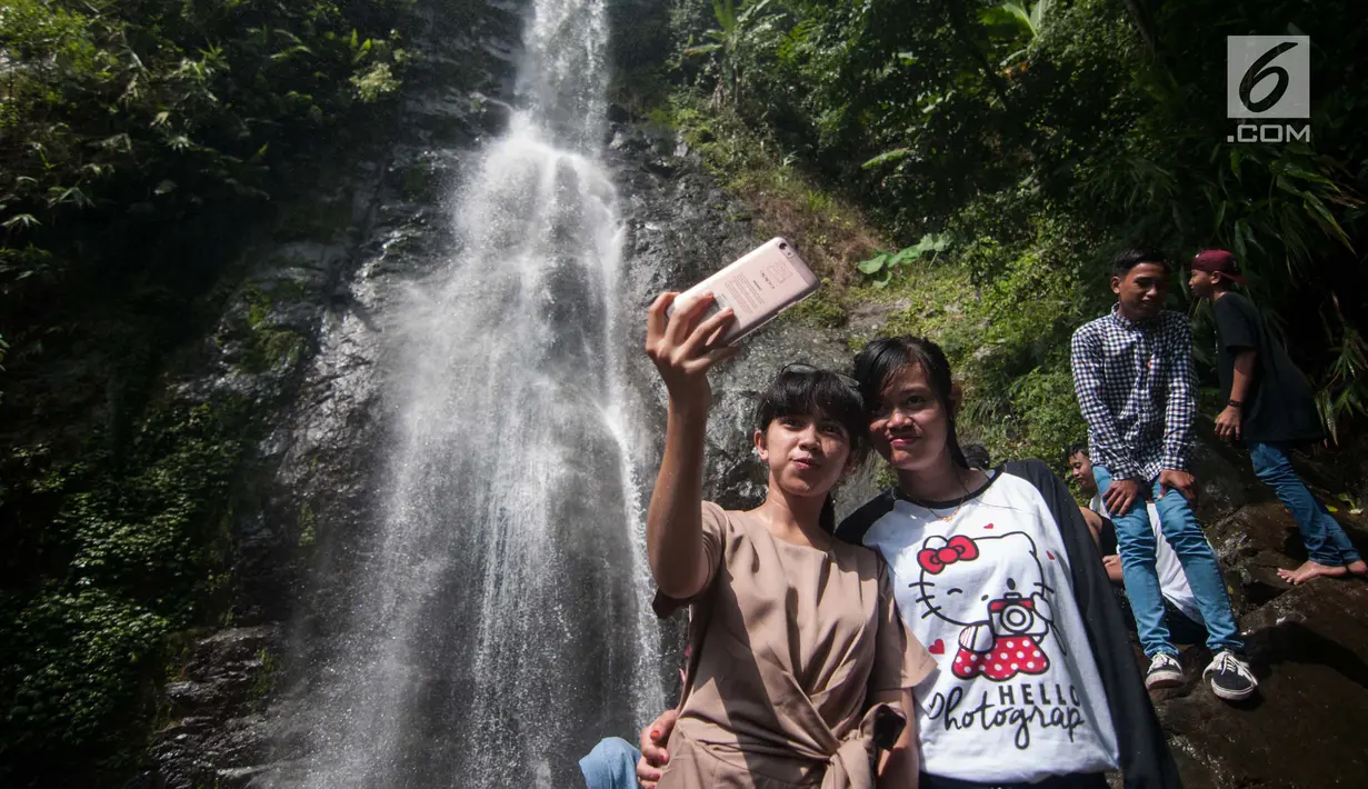 Wisatawan berswa foto di air terjun Cigentis, Kabupaten Karawang, Jabar, Kamis (29/6). Air terjun yang berada di kaki Gunung Sanggabuana tersebut menjadi salah satu tujuan wisata untuk mengisi libur lebaran. (Liputan6.com/Gempur M Surya)