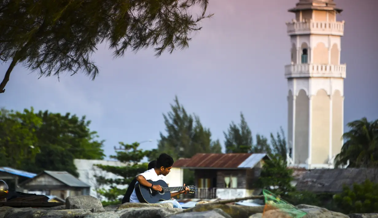 Seorang pria memainkan gitar sambil menikmati matahari terbenam di pantai di Banda Aceh (7/4). Sebagai pusat pemerintahan, Banda Aceh menjadi pusat kegiatan ekonomi, politik, sosial dan budaya. (AFP Photo/Chaideer Mahyuddin)
