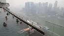 Warga berenang di kolam renang yang menghadap ke distrik pusat bisnis Singapura yang diselimuti kabut, Senin (14/9/2015). Singapura tak luput terkena dampak kabut asap pembakaran lahan di Pulau Sumatera. (REUTERS/Edgar Su)