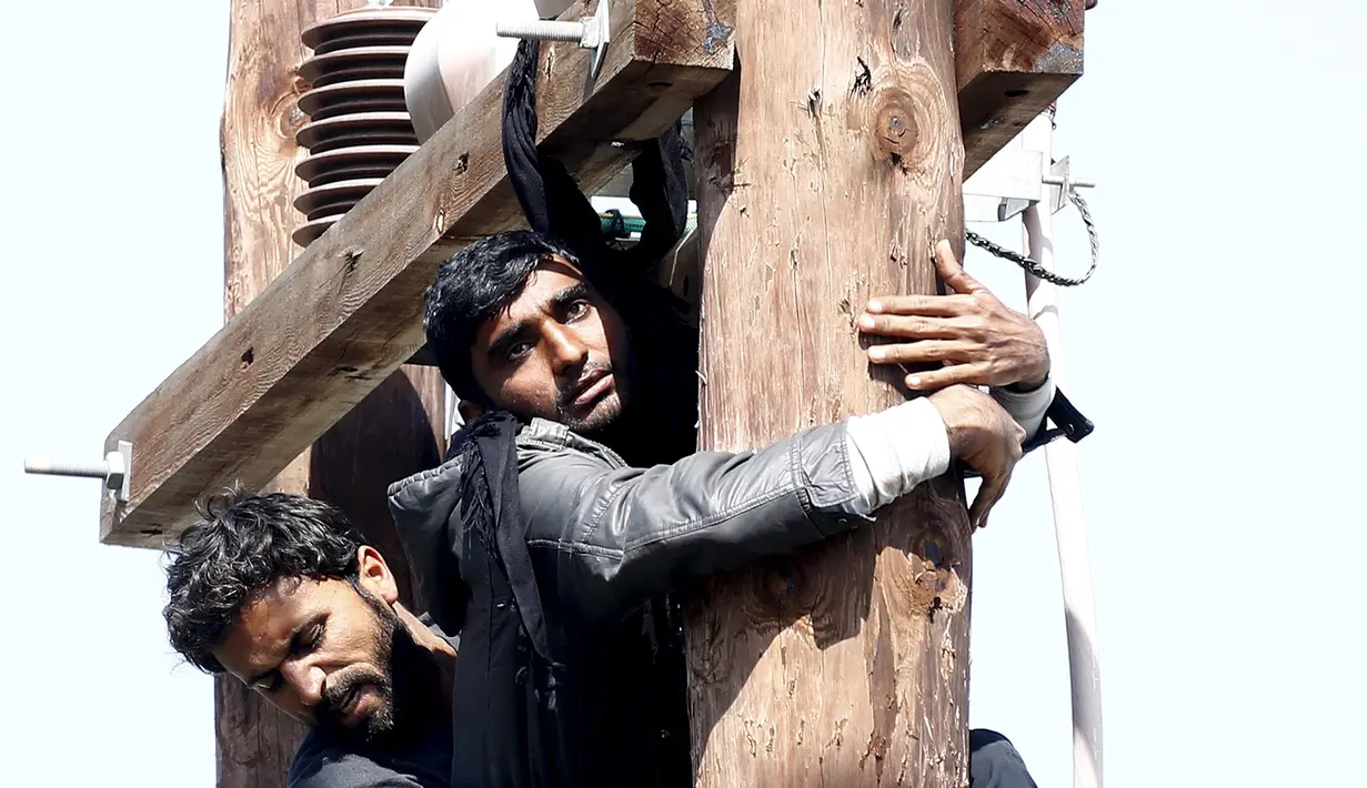 Imigran asal Pakistan (depan) saat mengancam akan menggantung diri di tiang listrik, Lesbos, Yunani, Rabu (6/4). Aksi tersebut dilakukan saat demo di pusat pendaftaran kamp pengungsi atau imigran di Yunani. (REUTERS / Giorgos Moutafis)