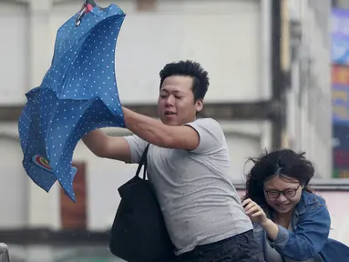 Dua orang memegang payung sambil berjalan menghindari angin kencang yang disebabkan topan Dujuan di Taipei, Taiwan, Senin (28/9). Ribuan orang diungsikan untuk menghadapi topan raksasa Dujuan yang diprediksikan akan menyerang Taiwan.(REUTERS/Pichi Chuang)