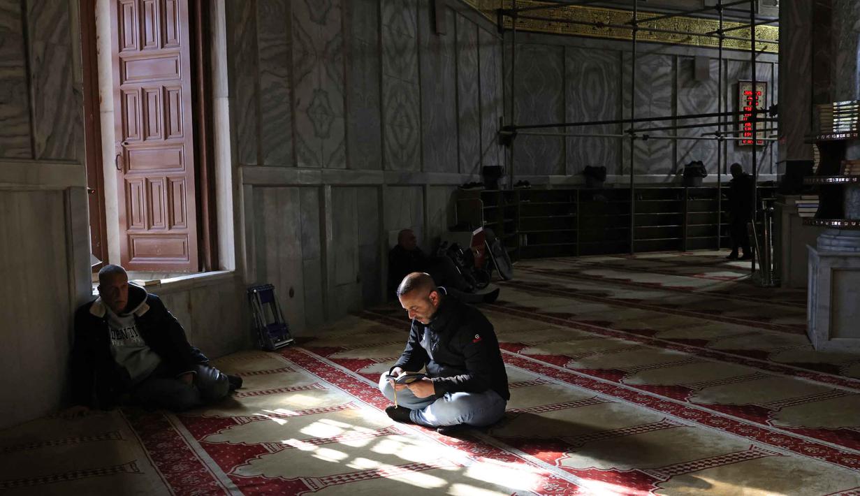 Secara harfiah, Kubah Shakhrah berarti “kubah batu”, ini adalah bangunan persegi delapan berkubah emas yang berdiri di tengah kompleks Masjid Al Aqsha di Yerusalem Timur. Tampak dalam foto, seorang pria Palestina membaca Al-Quran di dalam Kubah Batu, kompleks Masjid al-Aqsa, Yerusalem menjelang waktu berbuka puasa selama bulan suci Ramadan 1447 Hijriah pada Rabu 25 Februari 2026. (AHMAD GHARABLI/AFP)