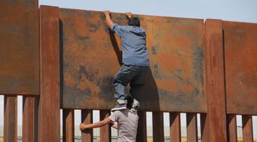 Seorang pemuda dibantu temannya memanjat tembok besi perbatasan antara Meksiko dan Amerika Serikat di negara bagian Chihuahua, Meksiko (6/4). Mereka menyeberang secara ilegal ke Sunland Park dari Ciudad Juarez. (AFP/Herika Matinez)