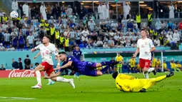 Pemain Argentina Nicolas Tagliafico (tengah) melompati kiper Polandia Wojciech Szczesny (kanan) saat mencoba untuk mencetak gol pada pertandingan sepak bola Grup C Piala Dunia 2022 di Stadion 974, Doha, Qatar, 30 November 2022. Argentina lolos ke babak 16 besar Piala Dunia 2022 dengan status juara Grup C usai mengalahkan Polandia 2-0. (AP Photo/Darko Bandic)