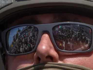 Para pengunjuk rasa yang memegang tanda dan bendera tercermin dalam kacamata yang dikenakan Garda Nasional California yang berdiri di luar Gedung Federal saat mereka memprotes operasi imigrasi federal di Los Angeles, Amerika Serikat pada 9 Juni 2025. (Apu GOMES/AFP)