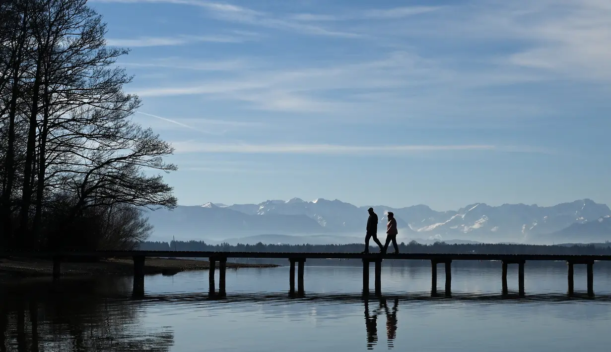 Pejalan kaki berjalan melewati panorama alpine di dermaga di danau Starnberger See dekat desa kecil Bavaria Seeshaupt, Jerman selatan (25/2). (AFP Photo/Christof Stache)