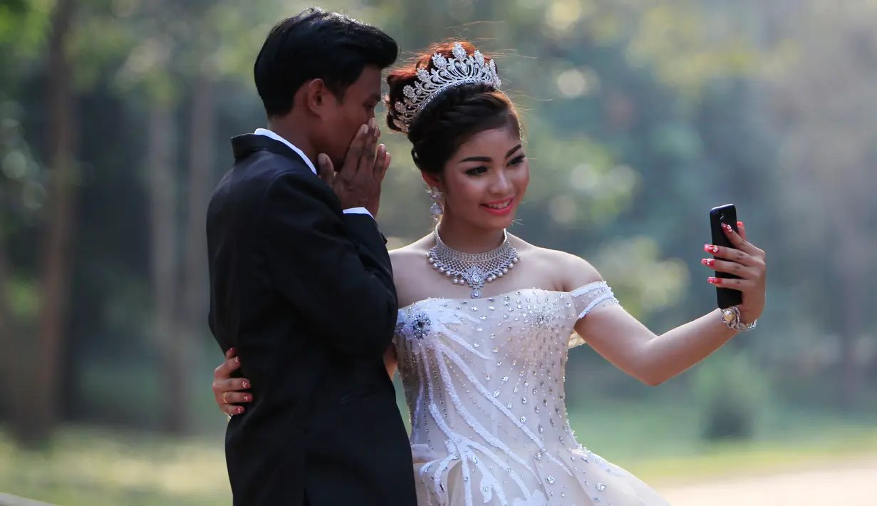 Sepasang pengantin baru berswafoto saat disela pengambilan foto pernikahan mereka di kompleks kuil Angkor Wat, sebuah candi ikonik dan bersejarah di Kamboja, 14 Maret 2018. Candi ini masuk dalam daftar Situs Warisan Dunia UNESCO. (AP Photo/Heng Sinith)