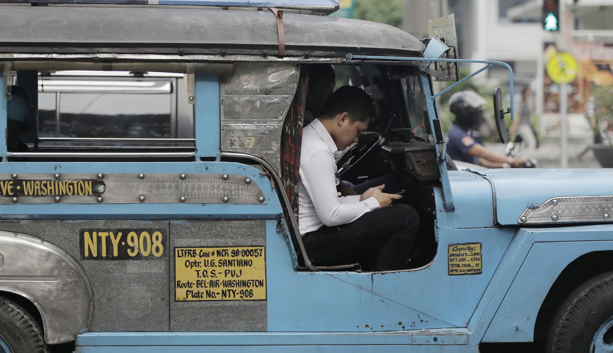 Pengemudi mobil Jeepney bermain handphone saat berada di Manila, Filipina, Jumat (22/11). Jeepney merupakan transportasi umum paling populer dan sudah menjadi ikon di Filipina. (Bola.com/M Iqbal Ichsan)