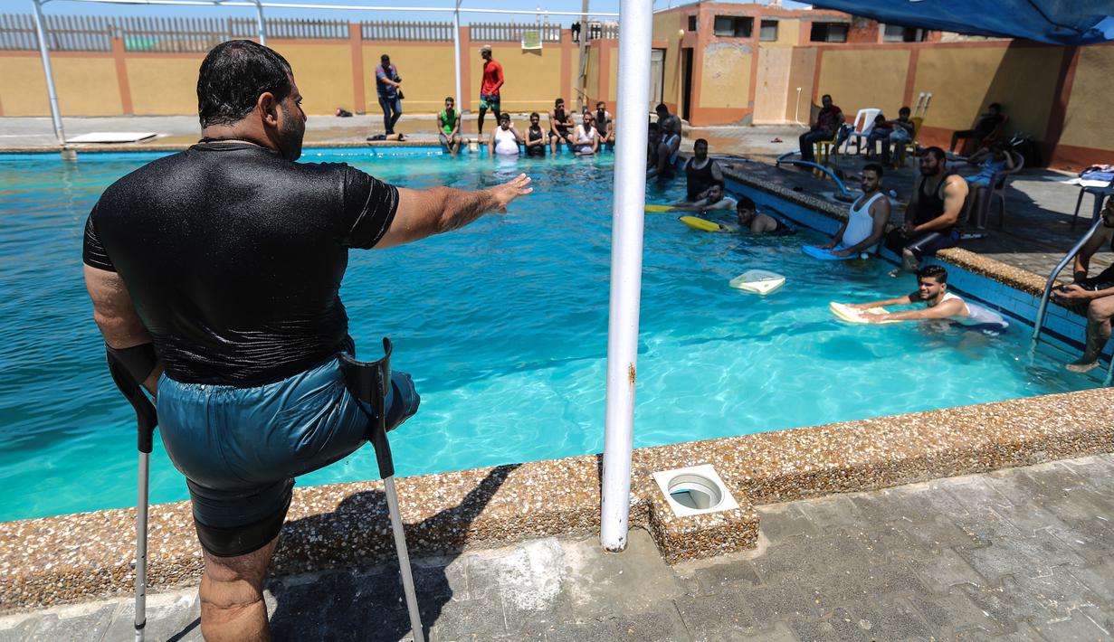 Majdi al-al-Tatar (kiri), instruktur renang saat melatih pemuda Palestina yang diamputasi di sebuah kolam renang di Kota Gaza (30/7/2019). Tatar melatih warga Palestina yang diamputasi untuk membantu mereka mempertahankan aktivitas fisik. (AFP Photo/Mahmud Hams)