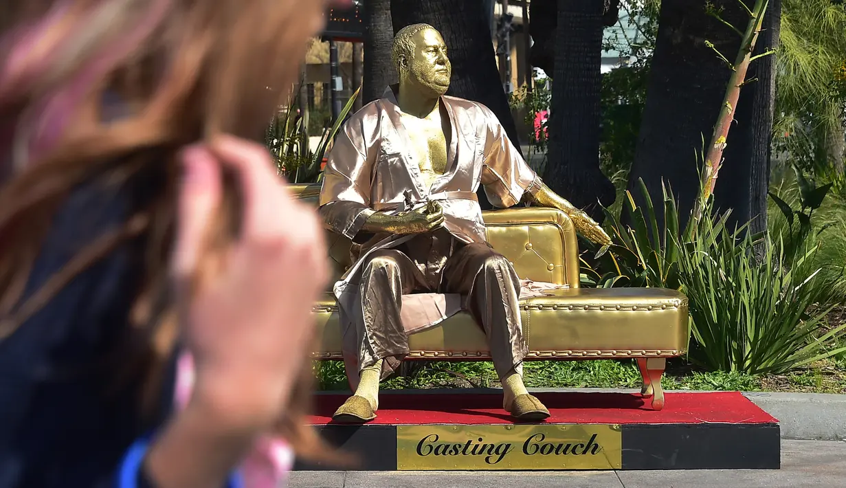 Seorang wanita berjalan dekat patung Harvey Weinstein yang dipajang dekat lokasi ajang Piala Oscar atau Academy Awards ke 90 di Hollywood, Kamis (1/3). Seniman Plastic Jesus memamerkan patung berjudul 'Casting Couch' tersebut. (Frederic J. BROWN/AFP)