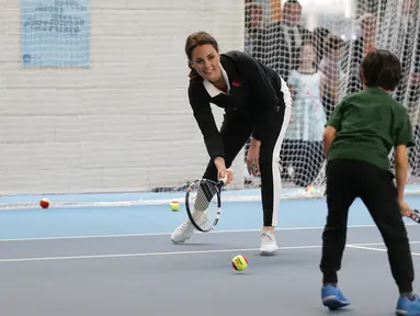 Kate Middleton berlatih bersama seorang anak saat mengunjungi Lawn Tennis Association di Pusat Tenis Nasional, London, Senin (31/10). Kate yang tengah hamil anak ketiga itu tampak mengenakan pakaian serba sporty. (Daniel LEAL-OLIVAS/POOL/AFP)