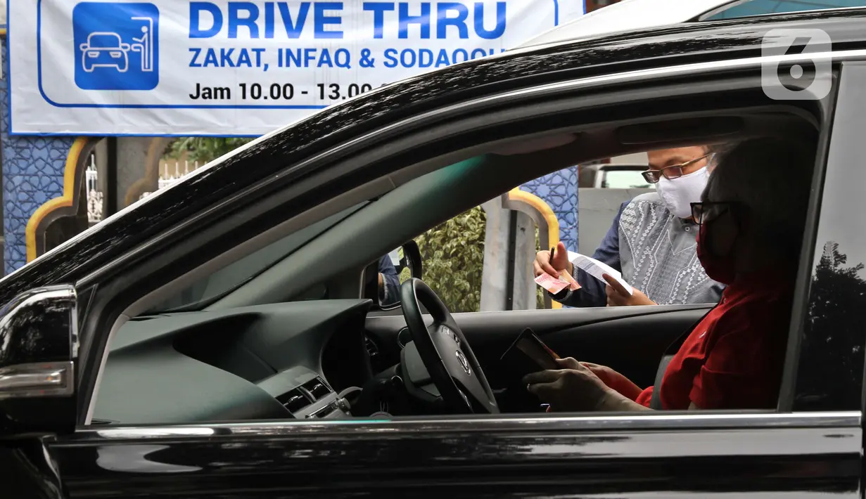Petugas Amil Zakat melayani warga yang membayar zakat fitrah melalui sistem "drive thru" di Masjid Nurul Hidayah, Tanah Kusir, Jakarta, Selasa (19/5/2020). Layanan zakat "drive thru" selama pandemi COVID-19 ini diberlakukan dengan protokol kesehatan dan keselamatan. (Liputan6.com/ Johan Tallo)