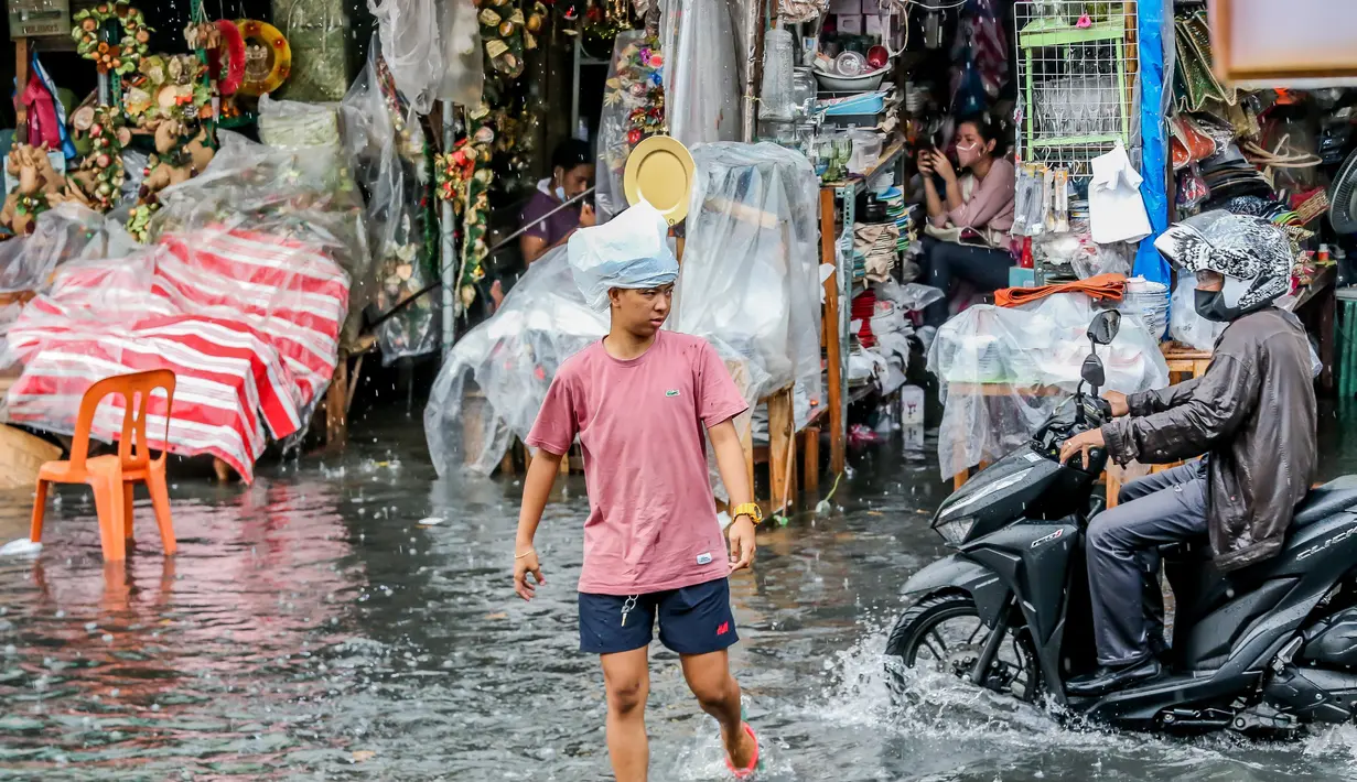 Seorang pria berjalan melewati banjir di tengah hujan deras yang tiba-tiba mengguyur di sebuah pasar dekorasi Natal di Manila, Filipina (9/12/2020). (Xinhua/Rouelle Umali)