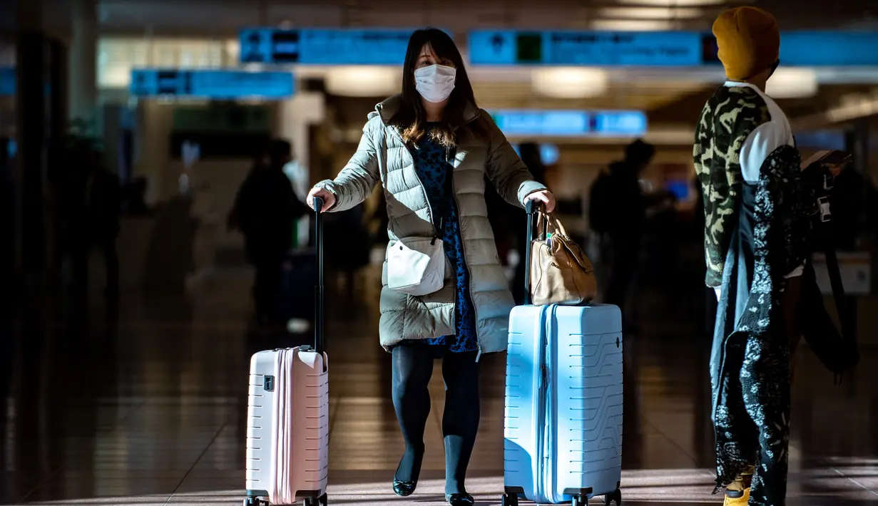 Seorang penumpang berjalan dengan kopernya di aula kedatangan di Bandara Internasional Haneda Tokyo, Jumat (18/2/2022). Pemerintah Jepang mengumumkan rencana untuk melonggarkan aturan perbatasan virus bagi pekerja dan pelajar. (AFP/Philip Fong)