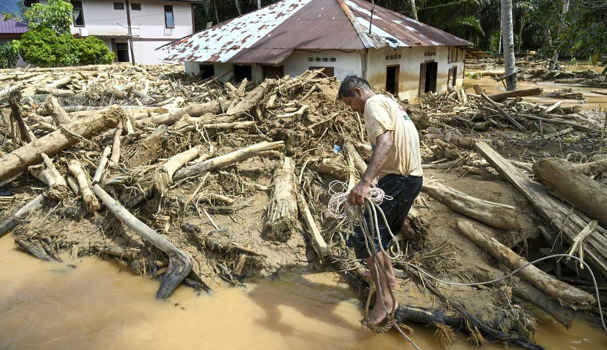 Hingga Selasa (2/12/2025), Desa Tukka, Tapanuli Tengah, Sumatera Utara masih tergenang banjir. Tampak dalam foto, seorang warga desa terdampak banjir bandang berjalan di antara tumpukan kayu di Desa Tukka, Tapanuli Tengah, Sumatera Utara, pada 2 Desember 2025. (YT HARIONO/AFP)